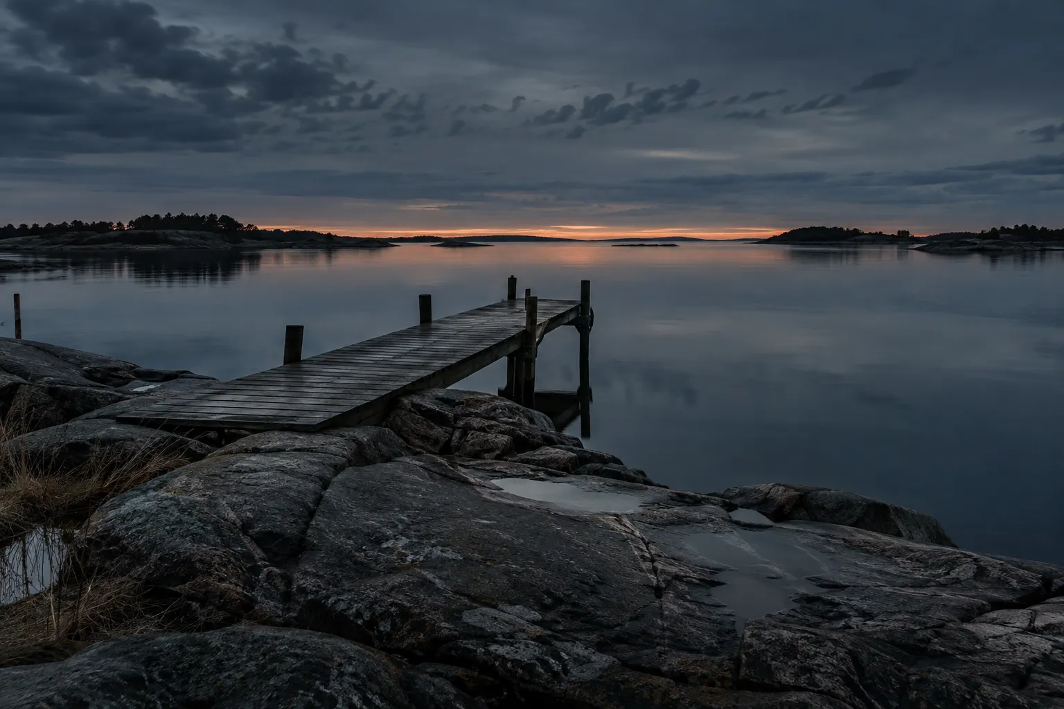 Wooden jetty leading into still water at blue dusk, with the last light on the horizon.